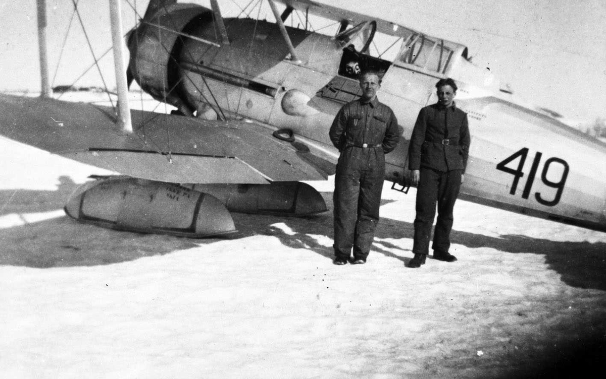 Norsk fly, dobbeldekker (Gloster Gladiator) på is. To mann står ved flyet.