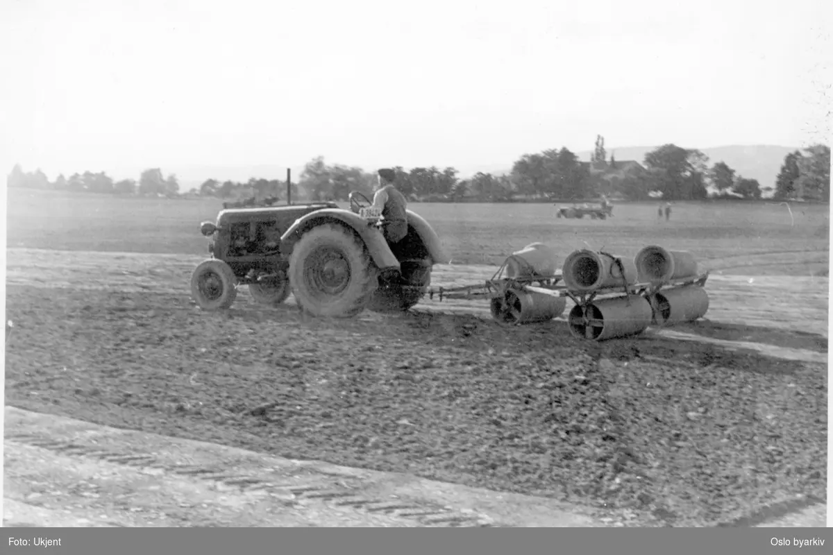 Traktor trekker ruller og rør på jorde på sletta.