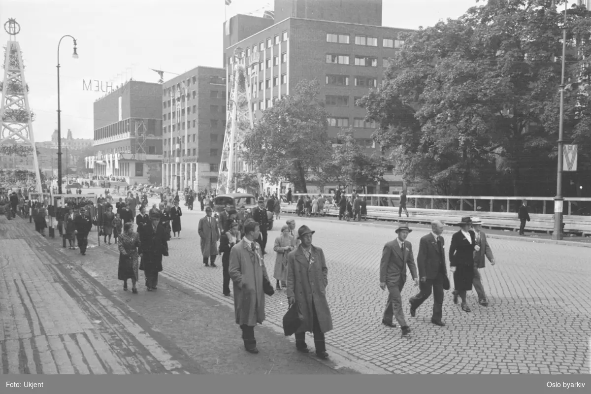 Folkevandring opp Rådhusgata fra Rådhusplassen 7. juni 1945, i anledning Kongens hjemkomst. Pyntede pyramidetårn. Rådhuset, forretningsbygg.