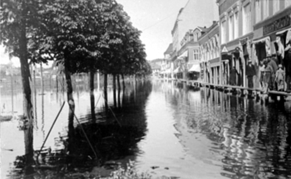 Mjøsflom, storflommen i 1927. Oversvømmelse i Strandgata, provisoriske fortau. Gutt med tærne i flomvannet er Eskild Johansen, bak står faren Rørlegger Ragnvald Johansen.