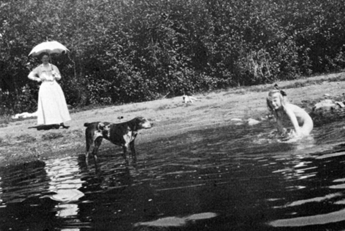 Margrethe Louise Kildal (Babs) f.1911 bader i Mjøsa. Hunden Peik ser på. Ukjent kvinne passer på. Hoel gård, Nes, Hedmark.