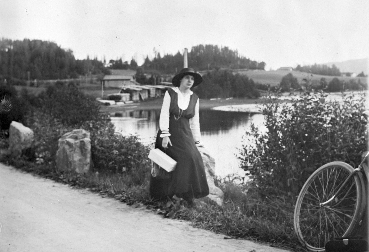 Frk. Brødrup på sykkeltur ved Korgerstuvika. I bakgrunnen Steinvik sagbruk som tilhørte Julius Olsen. 1924. 