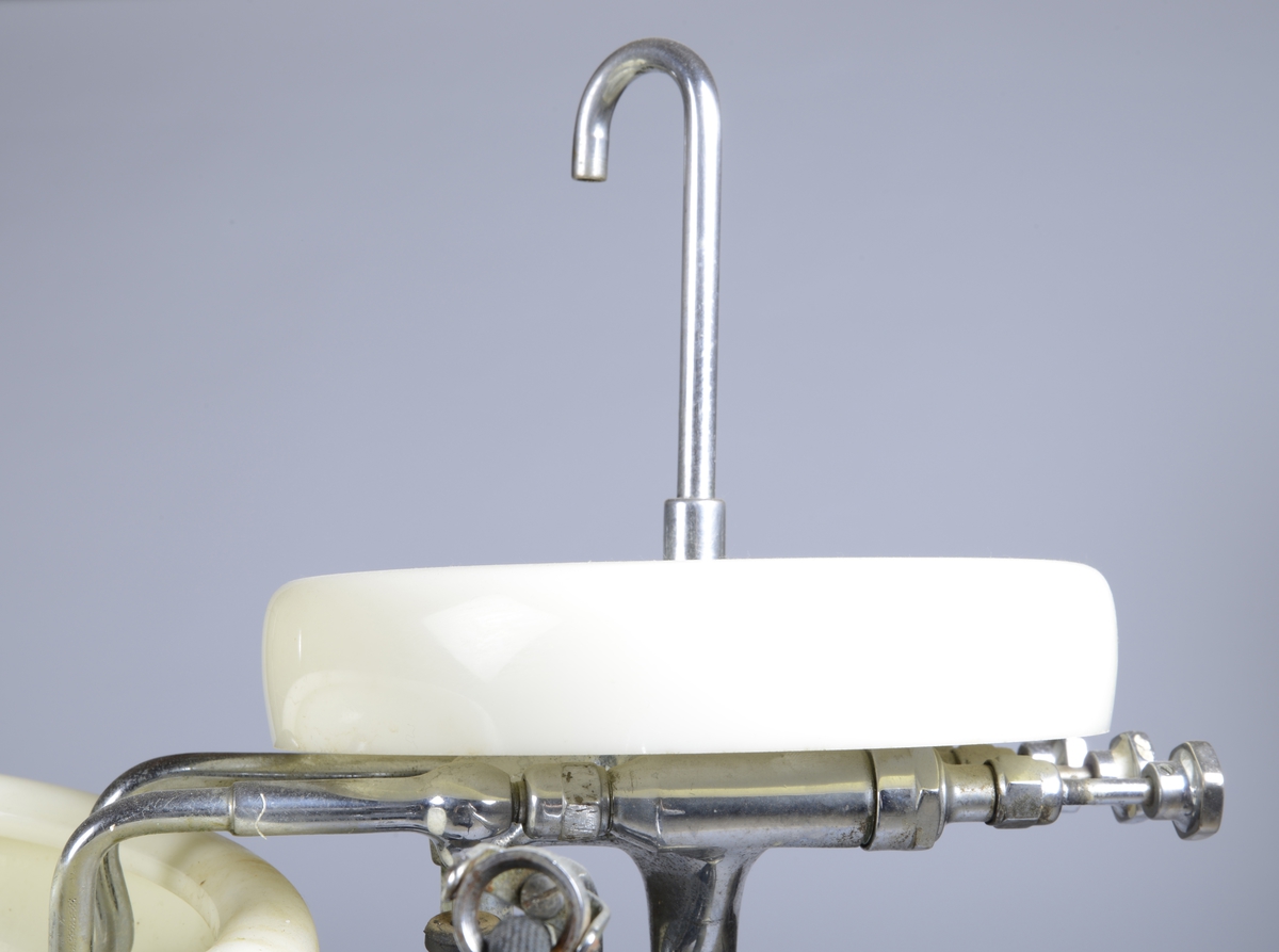 Dobbel vask på smal fot / stett til bruk på tannlegekontor ved behandlling av pasient. En liten øvre vask med liten kran, to rør fører vann til nedre vask som har sluk.