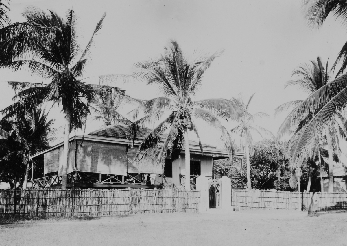 Mosambik. Bungalov i tre med veranda rundt huset. Utvendige "persienner" i bambus eller bast. Gjerde i bambus. 1914. Boligen kan være prefabrikert ved Thamshavn Bruk, Orkedalsøren.