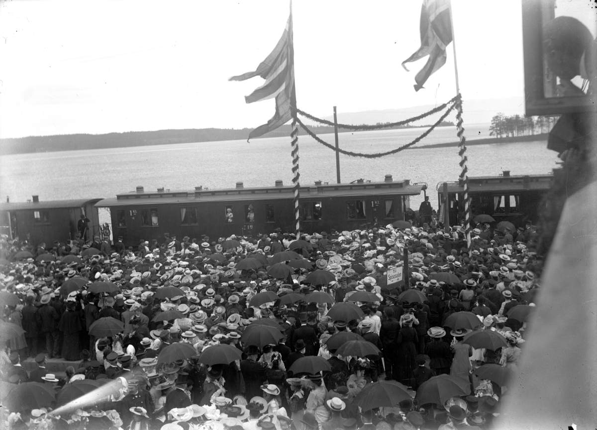 Hamar stasjon, kroningsreisen 1906, stor menneskemengde på perrongen, kong Haakon og dronning Maud ønskes velkommen, jernbanevogn, girlandere og flagg