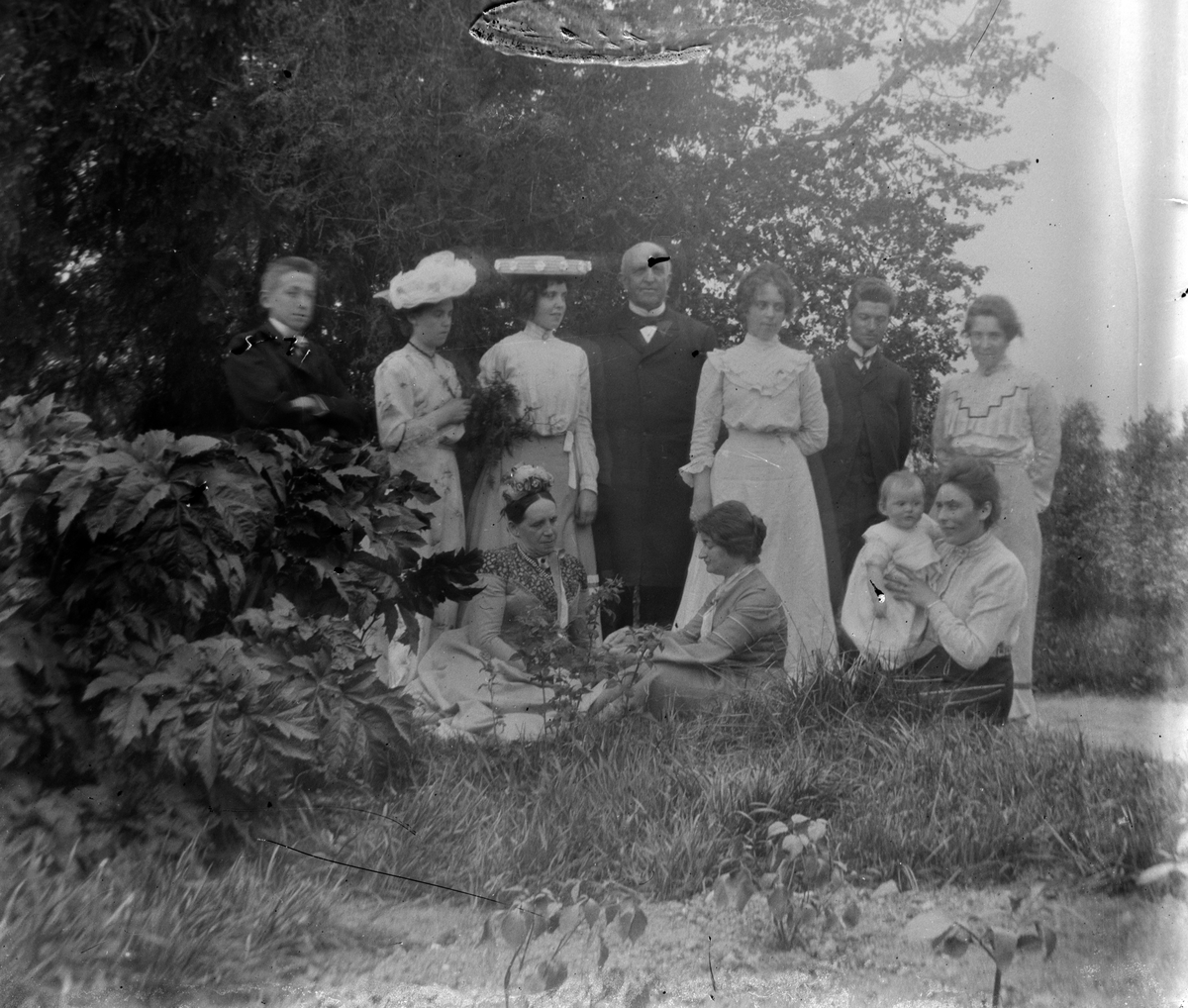 Familiegruppe i hagen på Hovinsholm gård, Helgøya i Ringsaker. Ukjente, bortsett fra Anna Hoel gift Ingier, sittende foran til høyre med datter Agnes på fanget. Bildet er fra 1903. Foto Jacob Hoel.