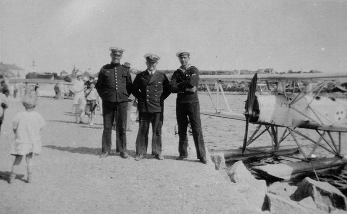 Tre militärer på en kaj bredvid flygplan Heinkel HD 25. Andra personer i bakgrunden.