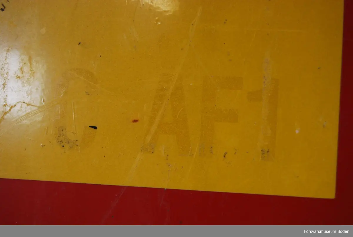 Gul och röd skylt av aluminium med två stolpfästen på den vinklade delen i över- och underkant. Bokstäver nertill i högra hörnet "C AF1" borttagna men märken från dem syns.