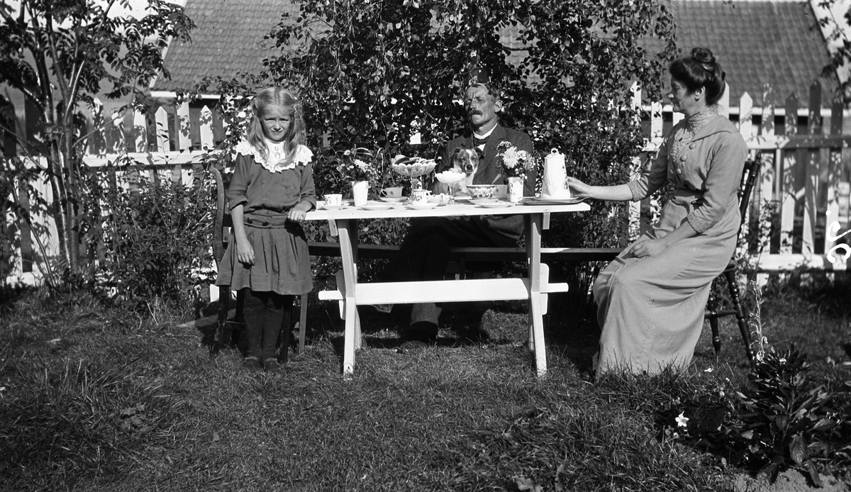 Utendørs kaffebord på gården Alm Øvre, Østre Toten. De to voksne er Ludvig Norli og hans hustru Petra, født Hoel. De eide gården. Jenta er deres pleiedatter.