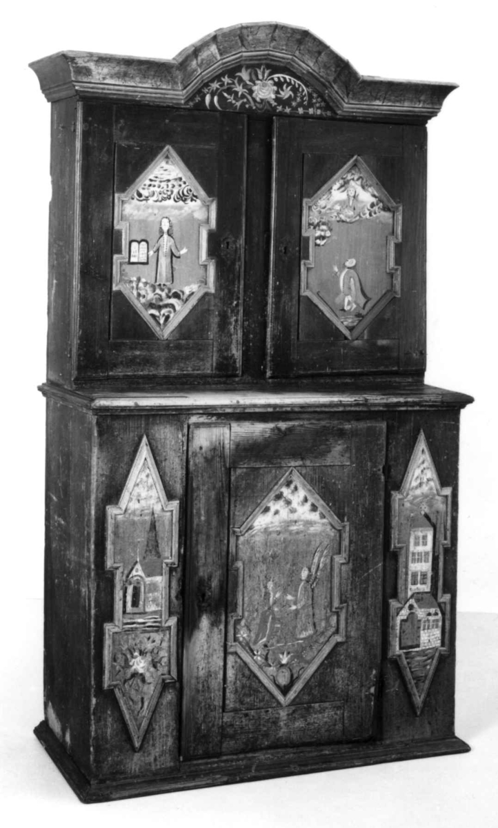 Skap, framskap i en del, to dører oppe og nede. Bibelske motiver; Moses og de ti bud. Gud på en sky, en brennede sky eller busk, en mann som har mistet en sko og en stokk.