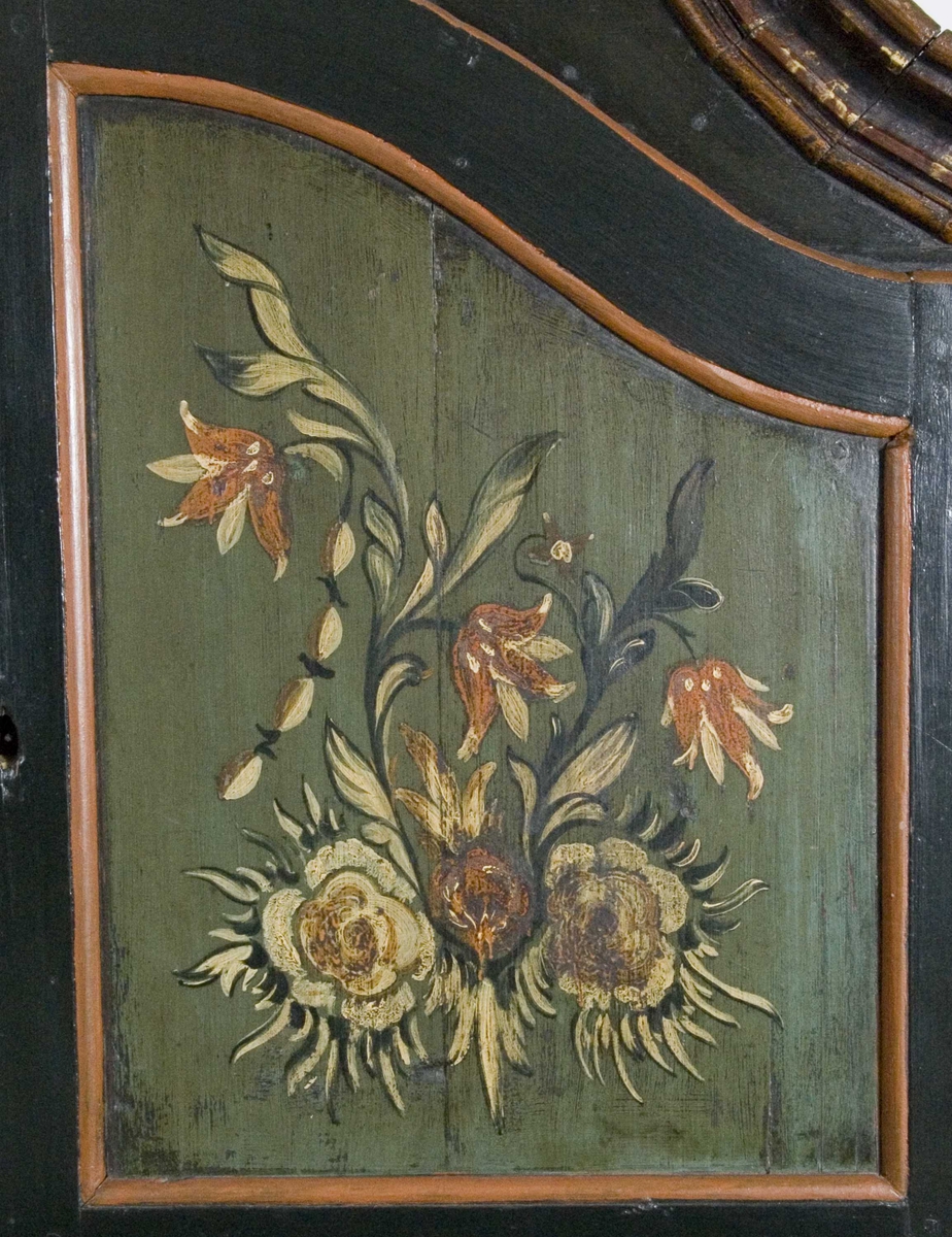 Skap i over- og underdel. Ovedelen har skjehylle og plass til skuffer. Buet topplist satt sammen av vinkelskårete deler. Blomstermalt.