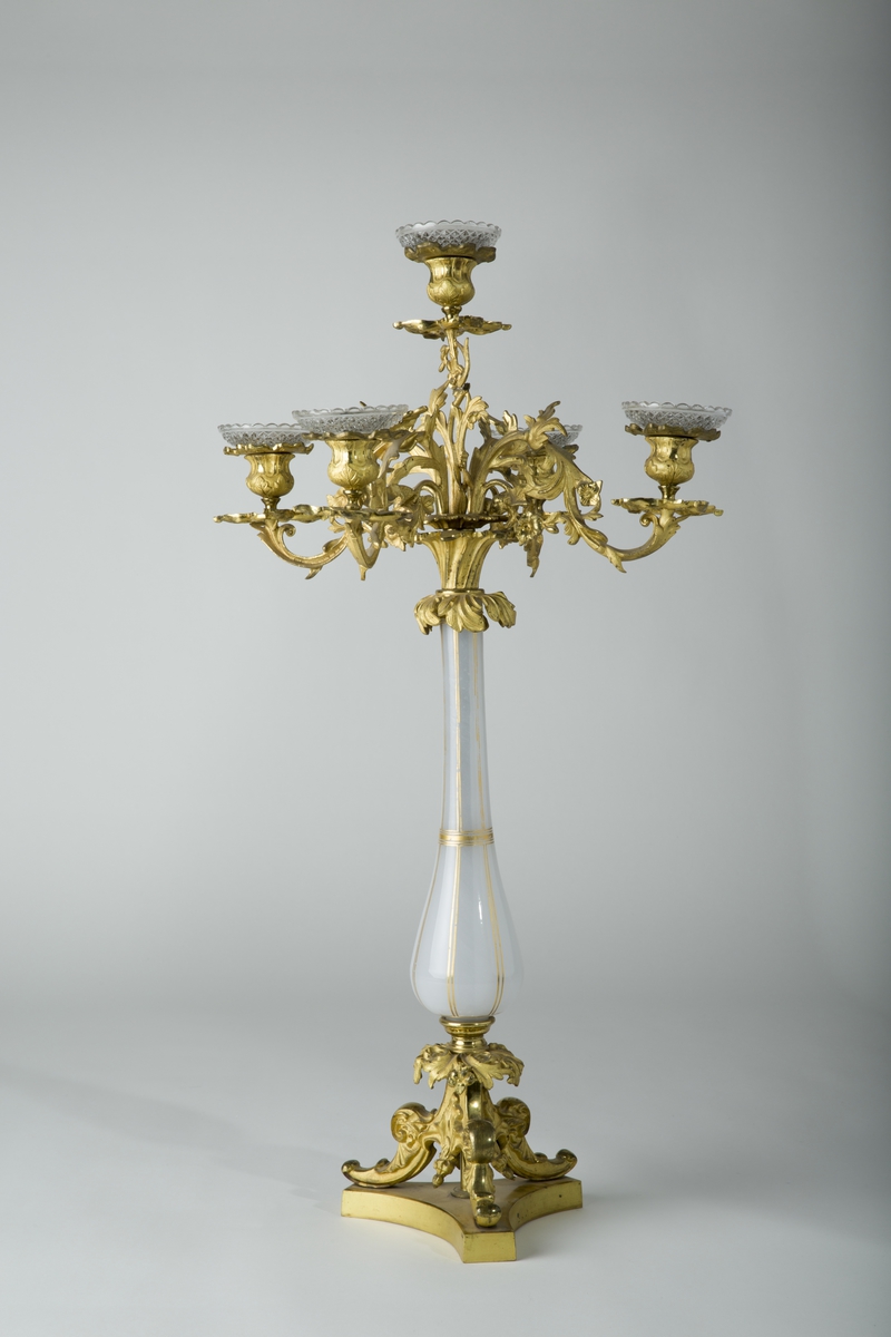 Kandelaber, bronse, forgylt; og mattglass med gull. 3 føtter på glatt Y-formet fot. Søylen av glass, pæreformet, øverst fem lysholdere i forgrenet bladverk.