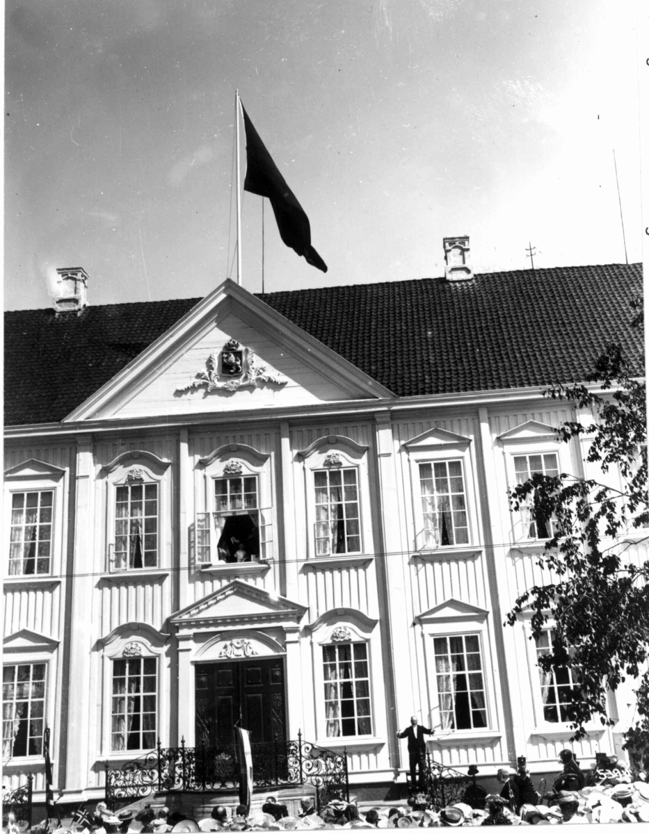 Stiftsgården i Trondheim i forbindelse med kong Haakon VII kroningsferd i 1906. Eksteriør med kronprins Olav i vinduet med flagg.