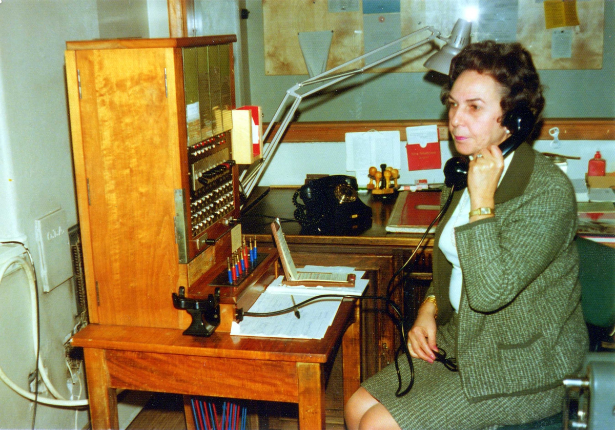 Berit Økern, ekstrahjelp på sentralbordet på Norsk Folkemuseum.
Her fotografert mens hun snakker i telefonen i desember 1974.