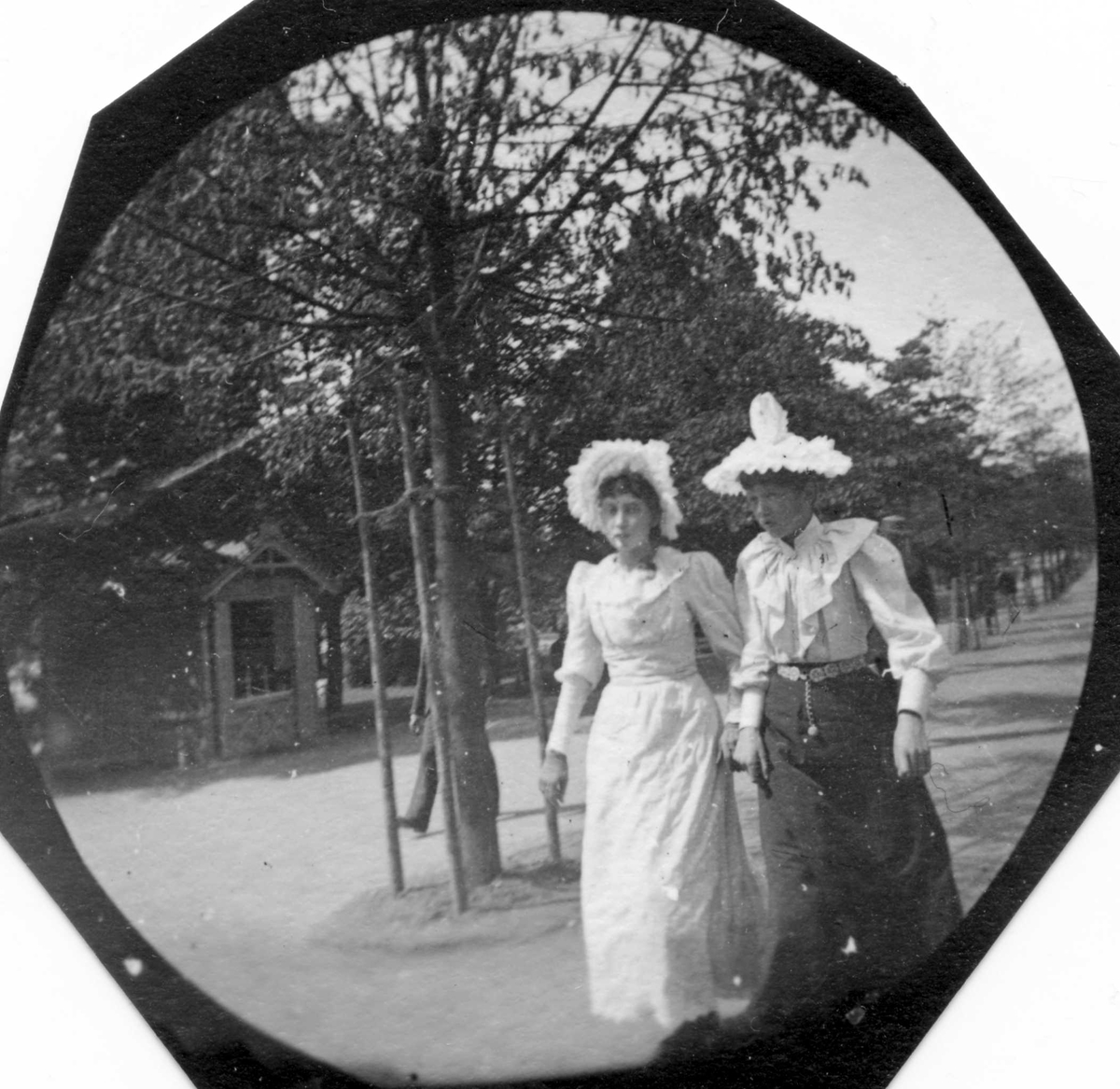 Frk. Holt og frk. Nielsen ("Molle" og "Polle") med hvite hatter spaserer ant. i Studenterlunden, Karl Johans gate, Oslo.