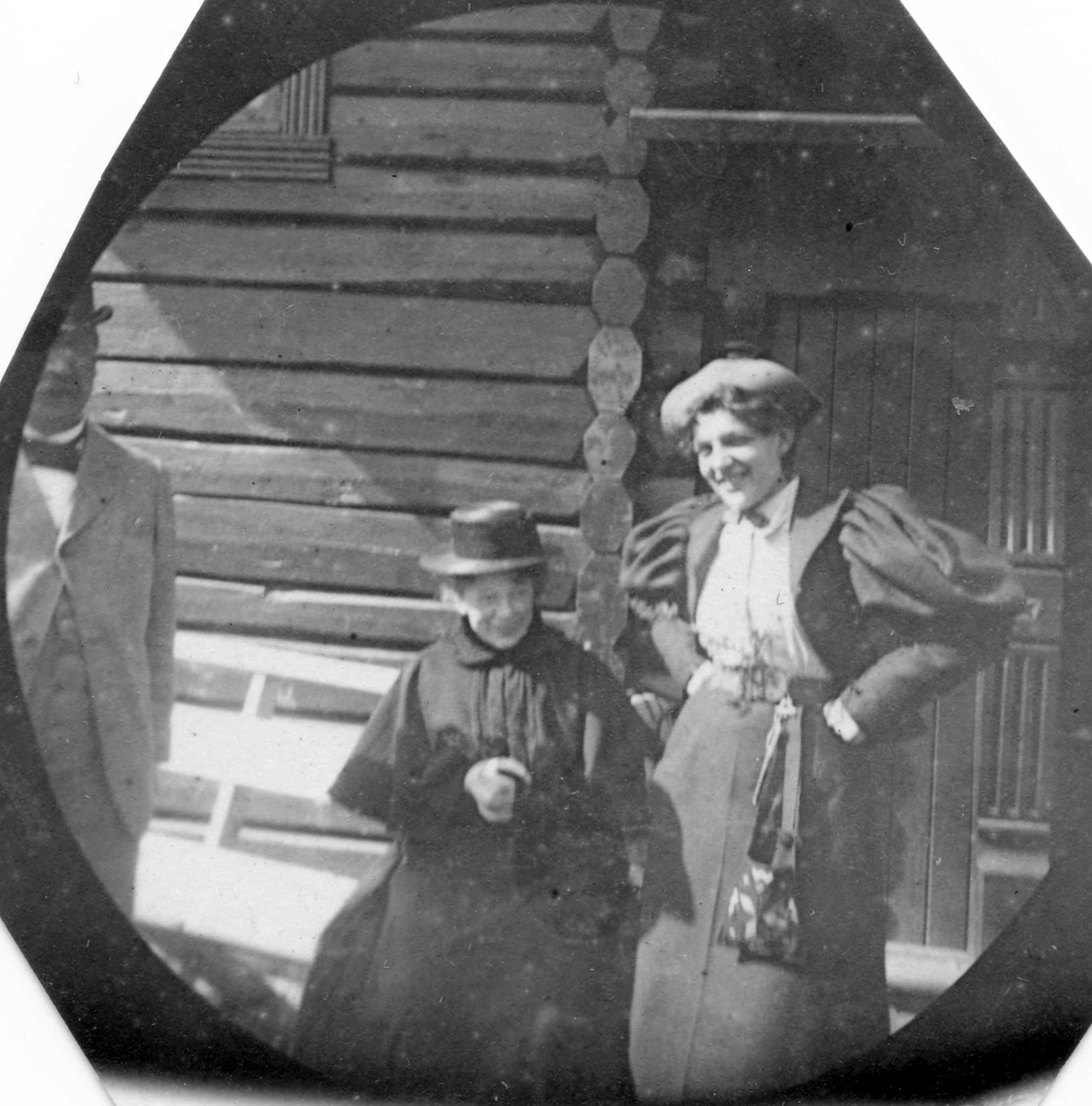 Golå, Sør-Fron, Oppland. En kvinne og en mann står foran tømmerhus. En kvinne sitter på en krakk.