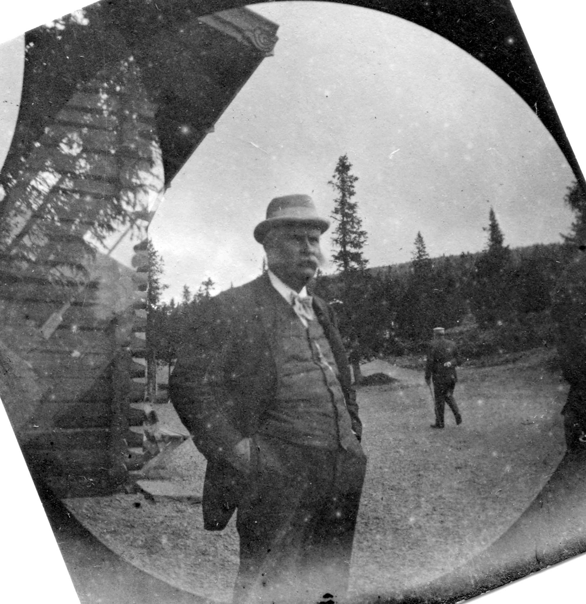 Golå, Sør-Fron, Oppland. Fotografens svigerfar, generalkonsul C. Clauson, med hendene i lomma ved tømmerhus i skogen.