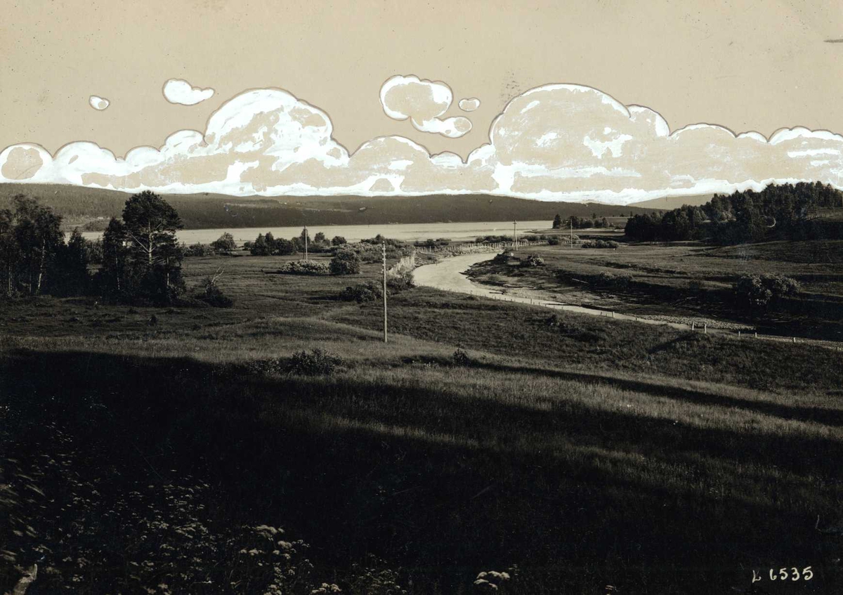 Hurdal, Øvre Romerike, Akershus. Utsikt fra veien ved kirken mot elv og Hurdalssjøen. Påmalte skyer.