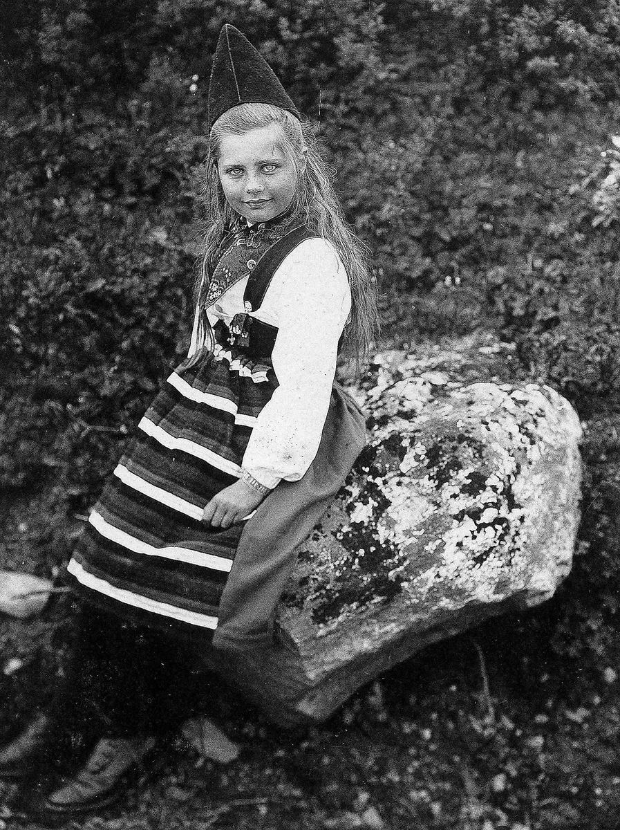 Pike ved stein, ukjent sted, i drakt fra Rättvik, Dalarne, Sverige.
Serie tatt av Robert Collett (1842-1913), amatørfotograf og professor i zoologi. 