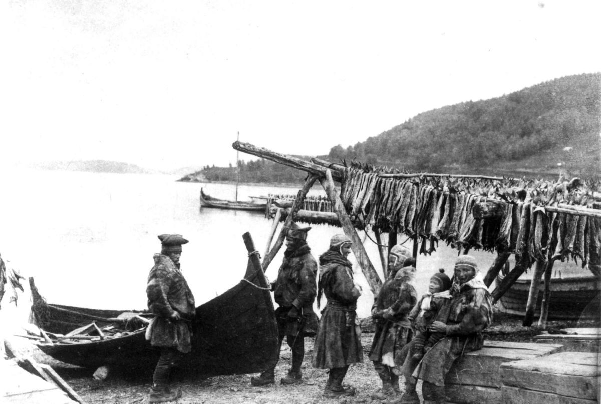 Karesuando-samer ved robåt på sommeropphold i Lyngseidet ca. 1884-90. I bakrunnen henger tørrfisk på et stativ kalt for hjell.