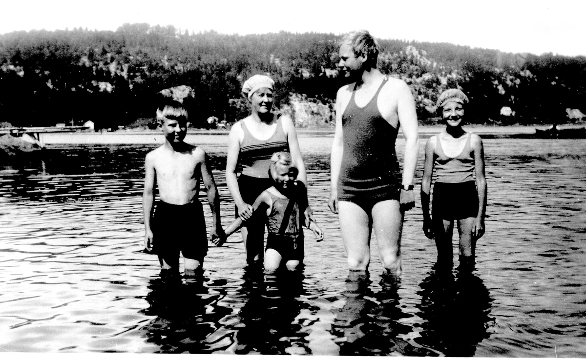 Barn og voksne som bader. Jorunn Fossberg på badestranden ved familiens sommerhus, Nærsnes, Røyken, Buskerud ca.1934, sammen med familiemedlemmer. 
Fra Jorunn Fossbergs familiealbum.