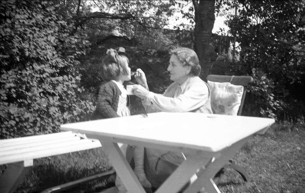 Nøtterøy 1939. Farmor Dikka Arentz og Kari ved et hagebord.  Farmor gir Kari noe å drikke.