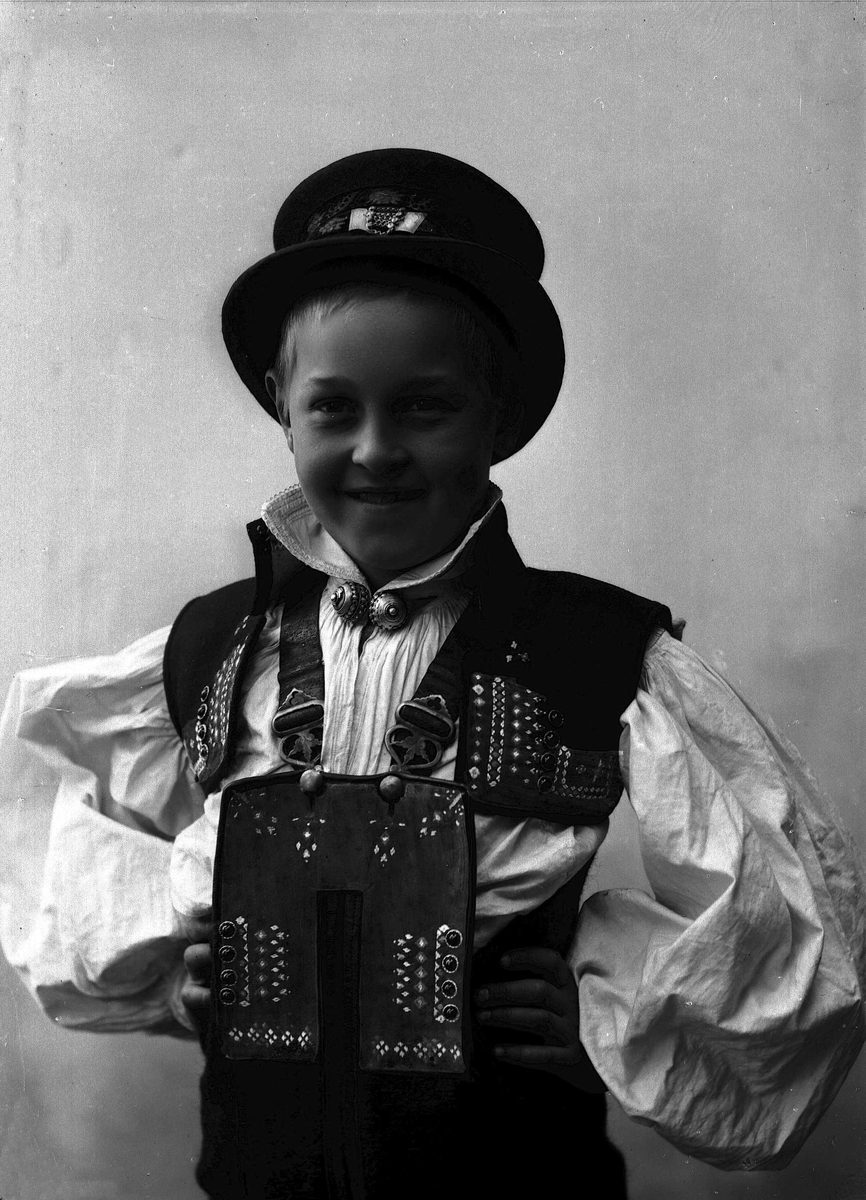 Studioportrett av ung gutt i drakt og hatt.