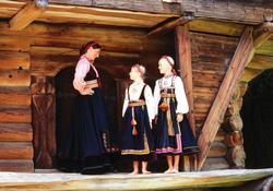 Kvinne og to jenter i telemarksbunad foran loftet fra Søndre