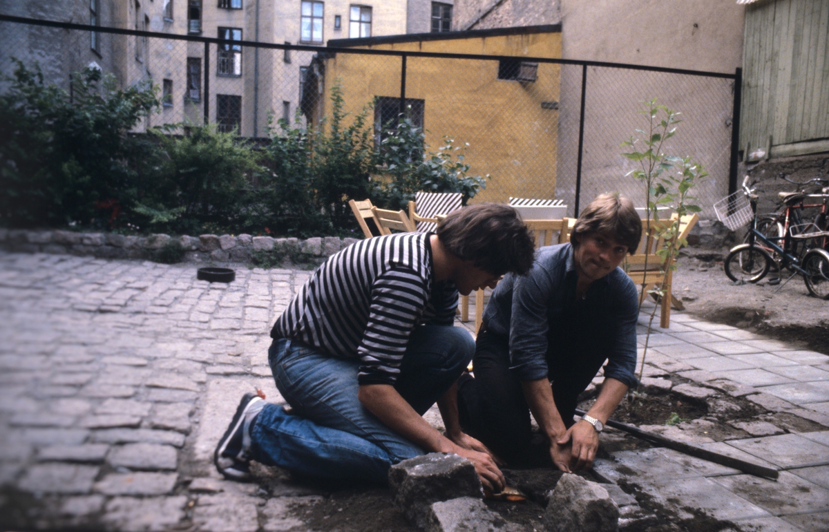To menn pynter med planter i bakgård. Bildet er antagelig tatt i forbindelse med en artikkel om byfornyelse på Grünerløkka i Oslo. Fotografert for Bonytt 1982.