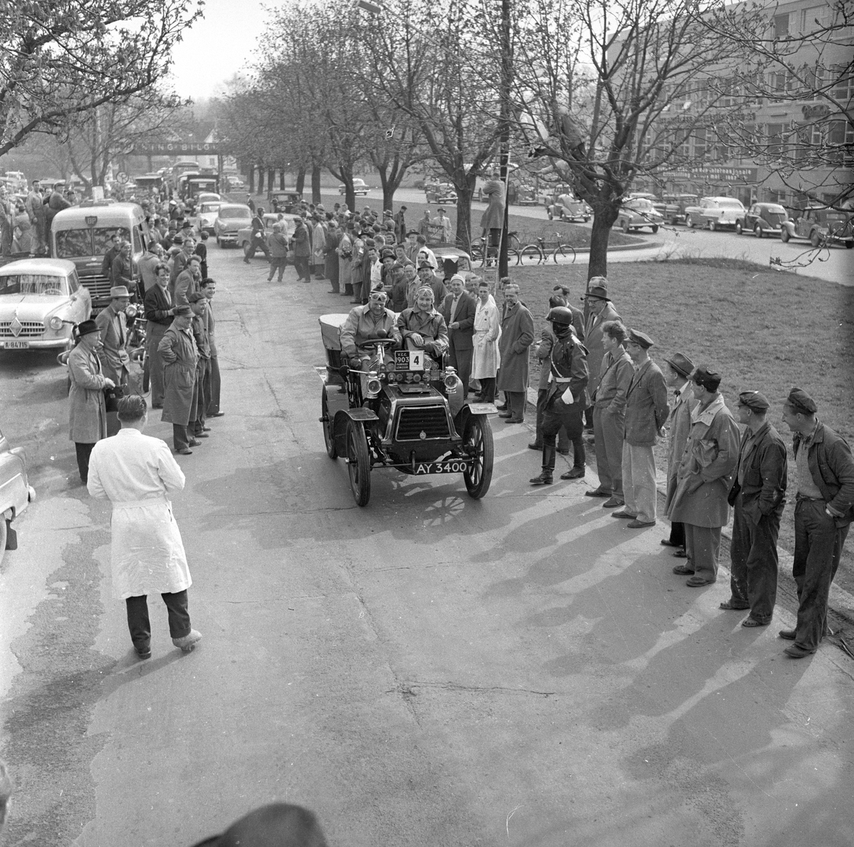 Veteranvogn Rally Oslofjord 1951. Sjåfør og passasjer kjører veteranbil. Publikum og politi langs traseen. Fotografert ant. 1951.