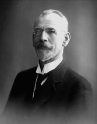 Portrett, mann med briller , skjegg og mørk dress. Skolebest