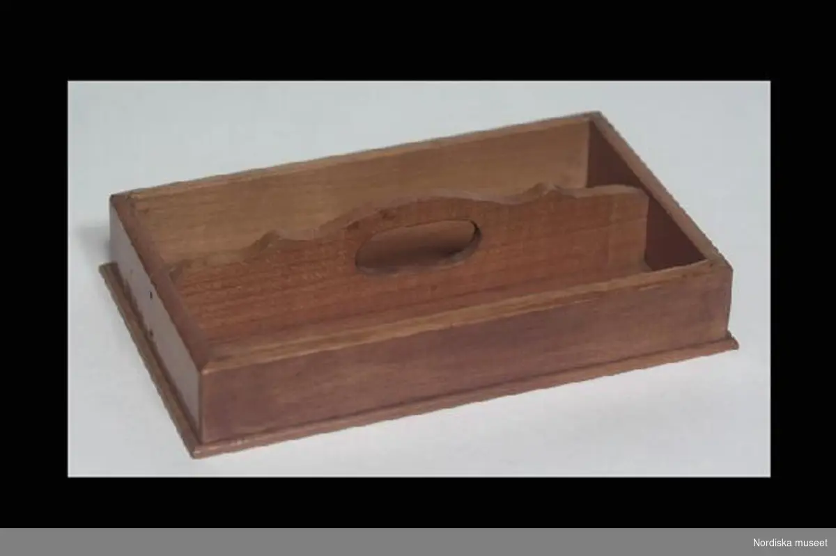Inventering Sesam 1996-1999:
L 18   B 10,5  (cm)
Skedlåda, leksak, av fernissat trä, rektangulär form, två fack som avskiljs av spjäla med utsågat handtag.
Använd i givarens hustrus familj i Schweiz.
Birgitta Martinius 1997