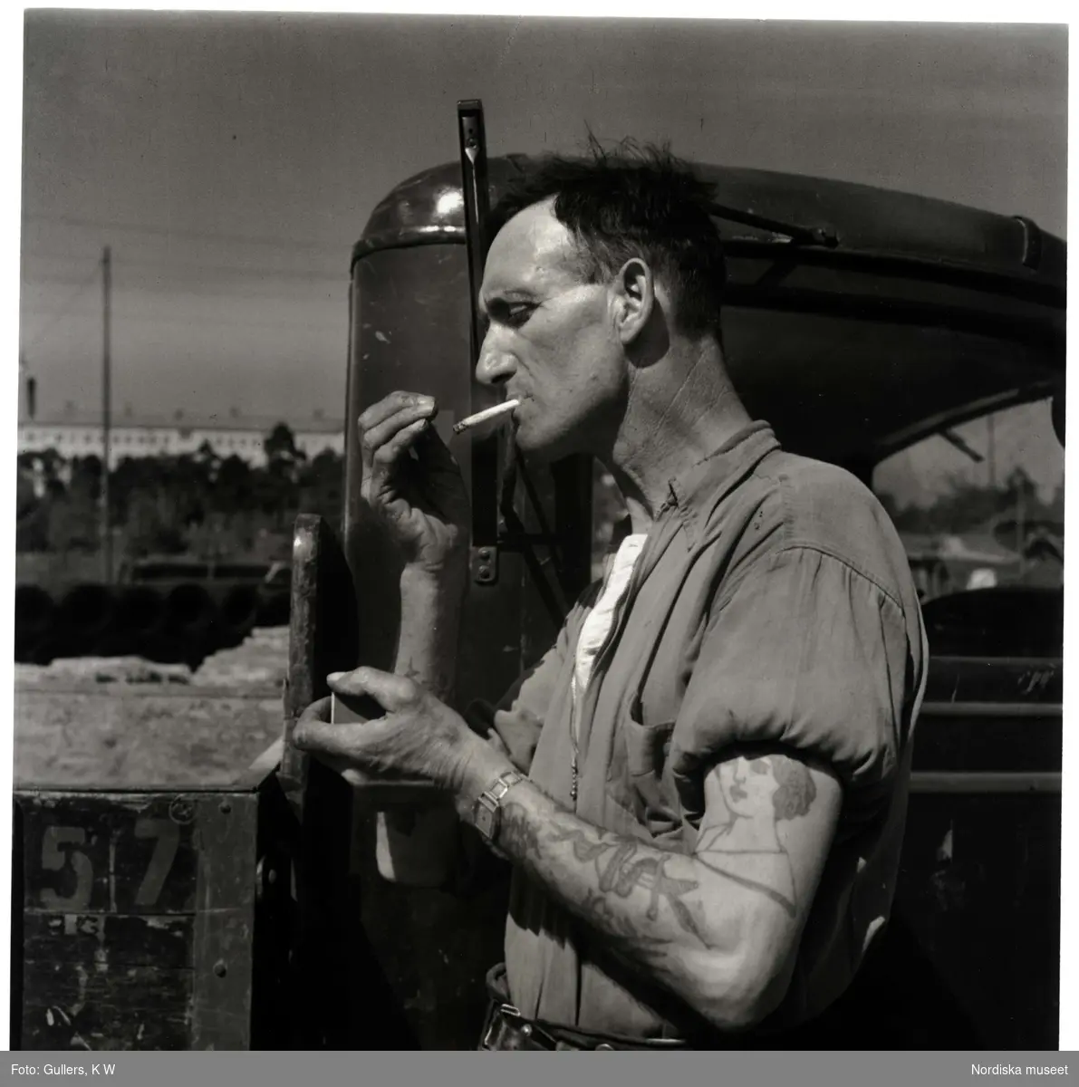 Lastbilschaufför med tatuerade armar tänder cigarett.