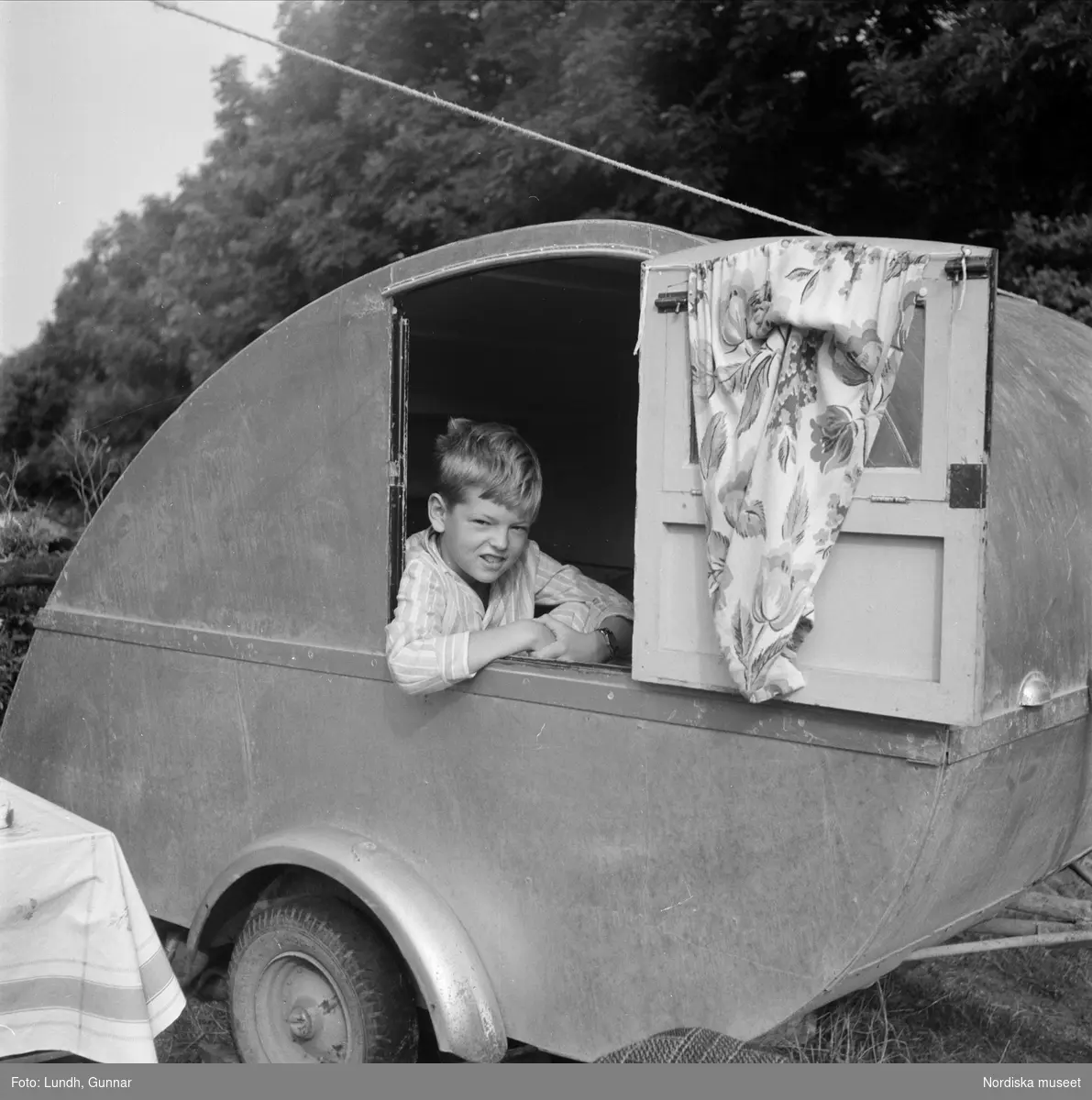 Mölle campingplats. Husvagn i träfanér. Pojke tittar ut ur husvagnsfönster.