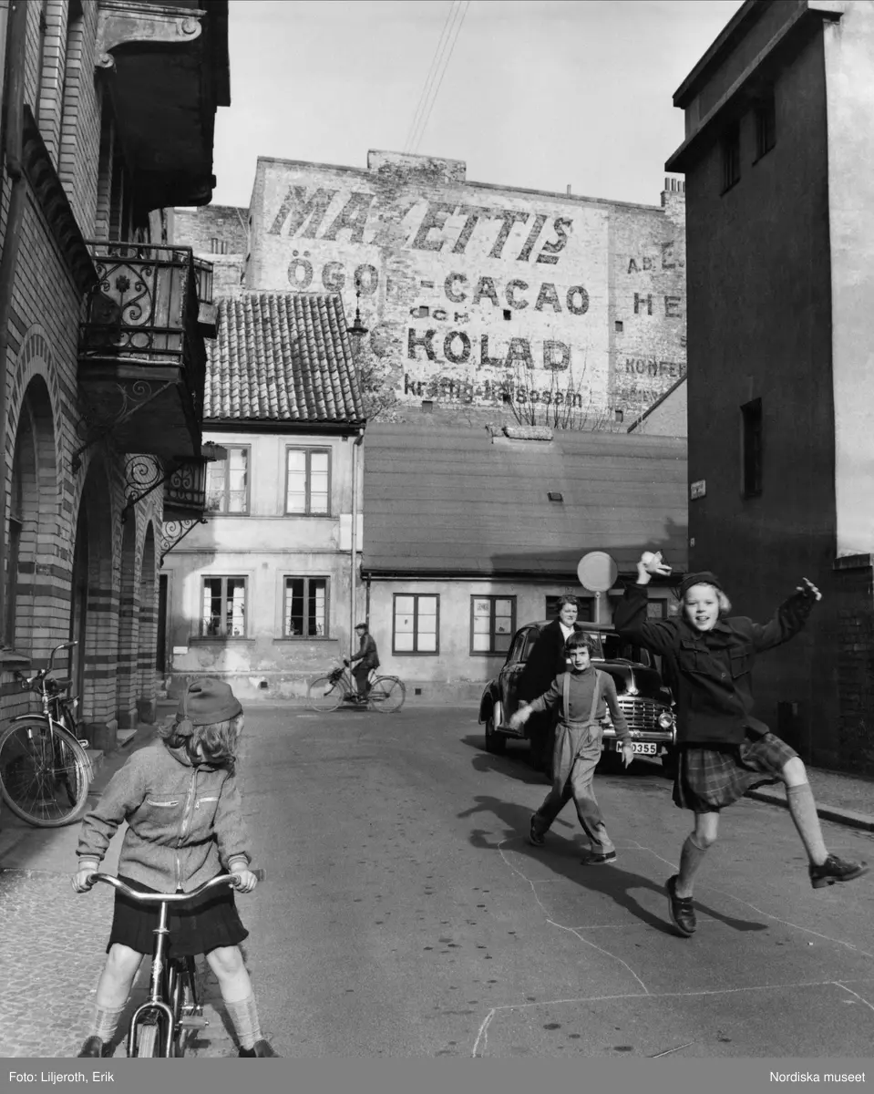 Barn som leker på en gata i Malmö. I bakgrunden reklam för Mazettis ögonkakao.