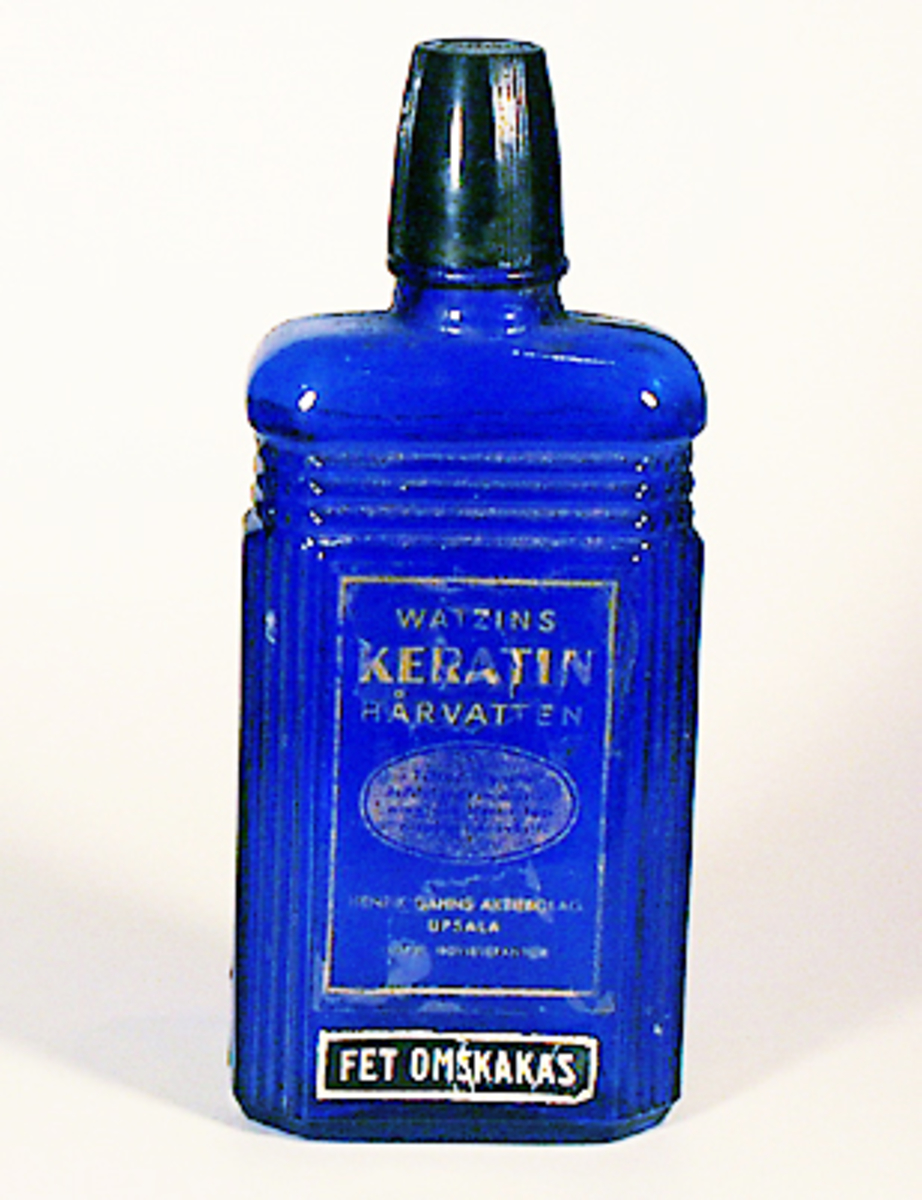Flaska av blått pressglas. Skruvhatt av svart plast. Genomskinlig etikett med guldtext "WATZINS KERATIN HÅRVATTEN. Henrik Gahns Aktiebolag, Upsala".