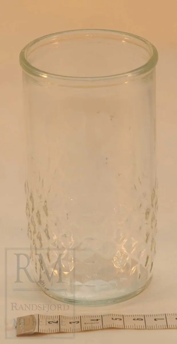 Sylinderformet glass, med kant øverst og dekorkant nederst. Opprinnelig lokk manger.