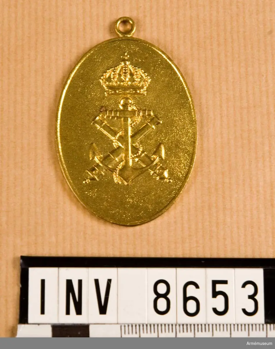 Höjd 55 mm. Bredd 40 mm. Vikt 27,7 g. Förgyllt ovalt märke med kustartilleriets emblem under kunglig krona. På frånsidan står i den övre kanten ORDNINGSBEFÄL och i den undre kanten MARINEN. Mitt på står det KFL 10. Upptill finns en ring.