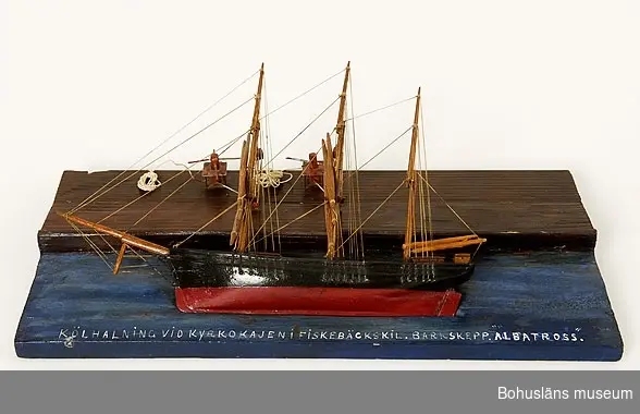 Modell av kölhalning av tremastade barken Albatross på Kyrkokajen, Fiskebäckskil. Tillverkad av kapten John Emil Olsson (1880-1950), Fiskebäckskil på Skaftö i Lysekils kommun på 1940-talet.
Trä, metall, lintråd, målat med oljefärg.
Fartygsmodell längd 30 cm, bredd 4 cm, höjd 20 cm. Platta: 40 x 19 cm; okänd skala. Blockmodell målad i  svart och rött. Stående och löpande rigg. Däckshus och lastluckor.
Monterad på en rektangulär platta med blåmålad vattenyta och brunmålad träkaj. Modellen ligger långsides med riggen nedhalad mot kajen. Två vinschspel på kajen fästade i fock- och stormast med två treskivade block i varje. Fällda rår. På modellens ovansida står textat med vita tryckbokstäver: 
KÖLHALNING VID KYRKOKAJEN I FISKEBÄCKSKIL. BARKSKEPP. "ALBATROSS".
Kölhalning innebär att skeppet krängs på sidan så att skrov, botten och köl kan repareras och underhållas.

Definitioner:
Bark - segelfartyg med tre eller fler master med rår på alla master och ett gaffelsegel på den aktra.
Råsegel - rektangulärt eller trapetsformigt segel som förs på en rå, dvs. en horisontell stång fäst vid mastens framkant
Gaffelsegel - trapetsformat segel fäst längs akterkanten av masten och med sina övre (kortare) och undre (längre) lik (kanter) fäst vid två rundhult (gaffel resp. bom).

Kyrkokajen eller Kyrkekajen, Fiskebäckskil:
Under segelsjöfartens storhetstid på 1860- och 70-talen fylldes Kilen på vintern av fartyg som låg uppankrade hemmavid. Det var på vintern man hade möjlighet att se över och underhålla fartygen inför nästa seglationsperiod.  Epoken varade fram till 1930-talet då segelskutornas tid var förbi. 
Vid Kyrkekajen ligger idag Skaftös skolsegelfartyg T/S Kvartsita.

Ur handskrivna katalogen 1957-1958:
Kölhalning av "Albatross"
Modell på platta. Kölens mått 19,5 Föremålet helt.
Från kapten Olssons saml., Fiskebäckskil.

För ytterligare information om John Emil Olsson och förvärvet, se UM005807.

Föremålet presenterat på Bohusläns museums hemsida år 2009 - 2013, webbutställning "John Emil Olsson Fiskebäckskils sjöfartsmuseum".
