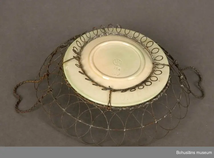 Assiett i keramik (majolika) på vilken satts ett kantgaller av järntråd.
Jämför UM18238.

Järnet rostat.