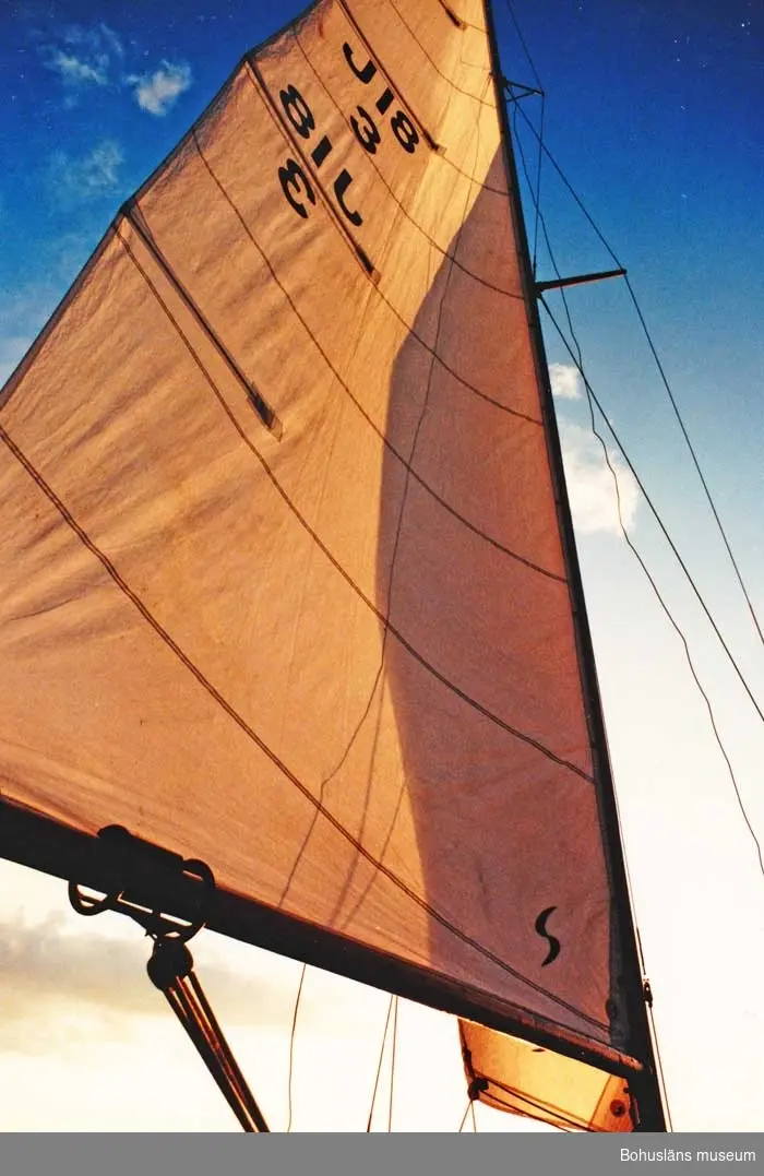 J18 kravellbyggd med ruff. Lackad, vit vattenlinje, rosa/svart bottenfärg.
Båten saknar mast och segel.
Fäste för utombordsmotor.