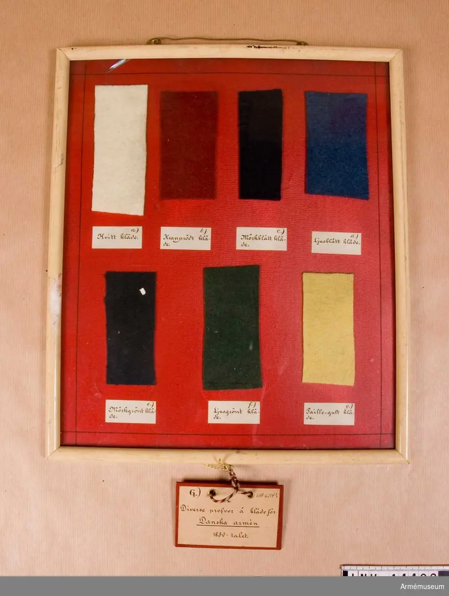 Grupp C I.
1830-tal.
Ram m 7 bitar av olika klädesprover och färger under glas. Bitarna är fastklistrade på röd kartong. Provfärgerna är: vitt, krapprött, mörkblått, ljusblått, mörkgrönt, ljusgrönt, paille gult.