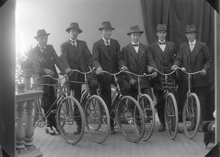 Sex män porträtterade tillsammans med sina cyklar i en fotoateljé