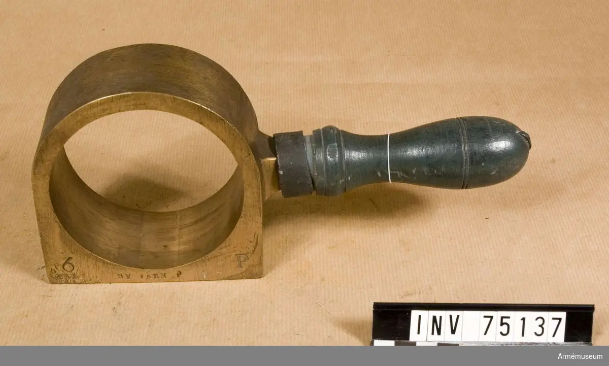 Grupp F:III(överstruken) V. 
Schamplun av metall med handtag av trä för prövning av färdiga karduser eller skott av 6-pundig kaliber.
