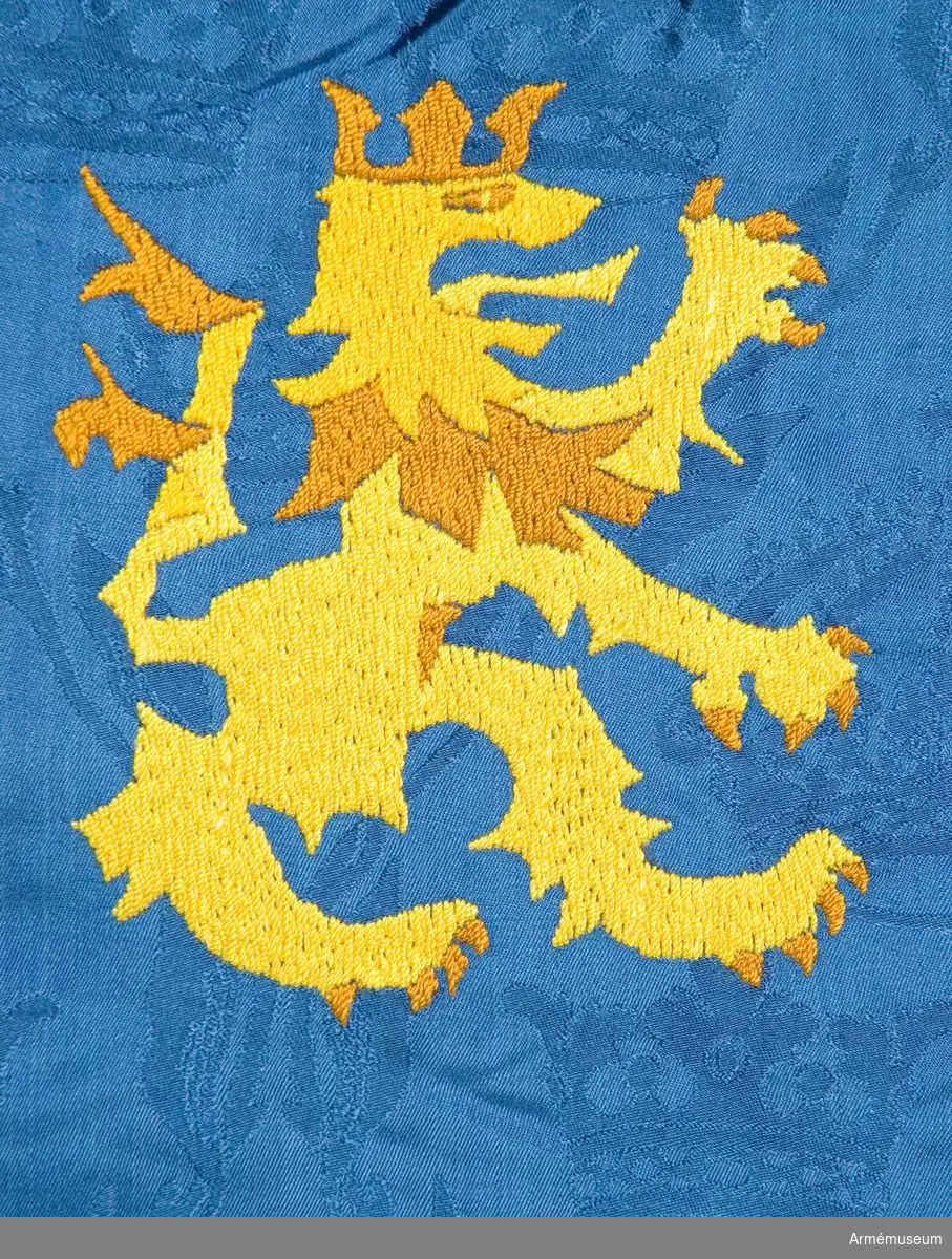 På blå duk ett stolpvis ställt gult svärd, i övre inre hörnet ett med öppen krona krönt upprest gult lejon. Duken av damastvävt fansiden. Motivet handbroderat i intarsia. Tillhörande spets, skyddsduk och fodral. Sidenet vävt av Almgrens sidenväveri
