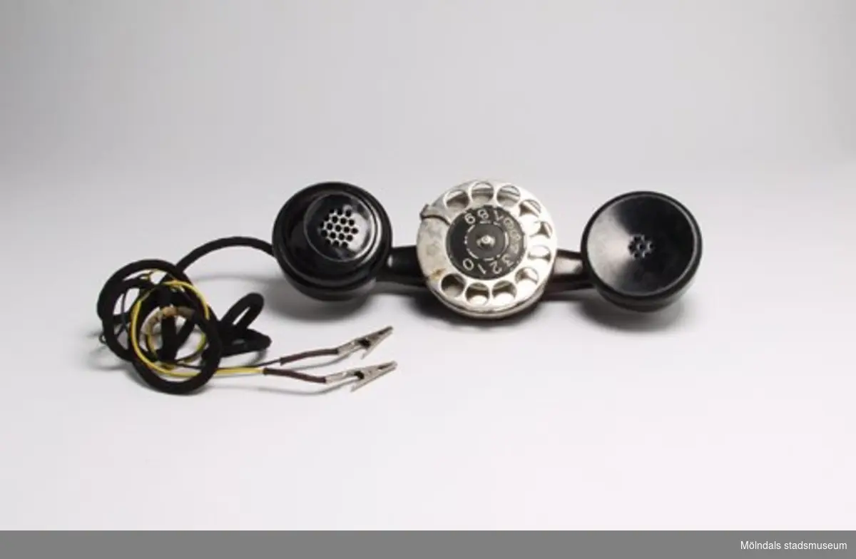 Telefon, lur med nummerskiva som används för direkt koppling i telefontråd i stolpe. Sladd med elektrodklämmor.
Arne arbetade som televerksarbetare fram till 1949, senare brandman (1949-1988). 
På kanten av nummerskivan står: Telefon A-B L.M. Ericsson, Stockholm 3349.