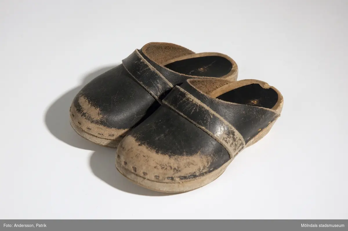 Ett par svarta träskor i barnstorlek från 1970-tal.I skon, vid hälen sitter en svart klisterlapp som utsmyckning och skydd.Skorna är något slitna.MåttLängd: 141 mm, Bredd: 65 mm, Höjd: 68 mm,  Storlek: 22 (?).Den vanligaste modellen av träko i Sverige är den med sula i trä och ovandel i läder. Äldre modeller är vanligen helt i trä och efterliknar skor av läder.