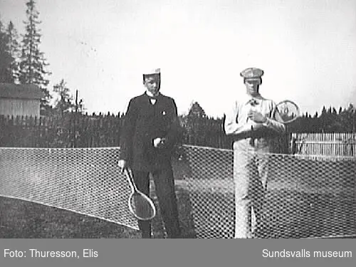 Två män vid tennisnät med tennisrackets i handen.