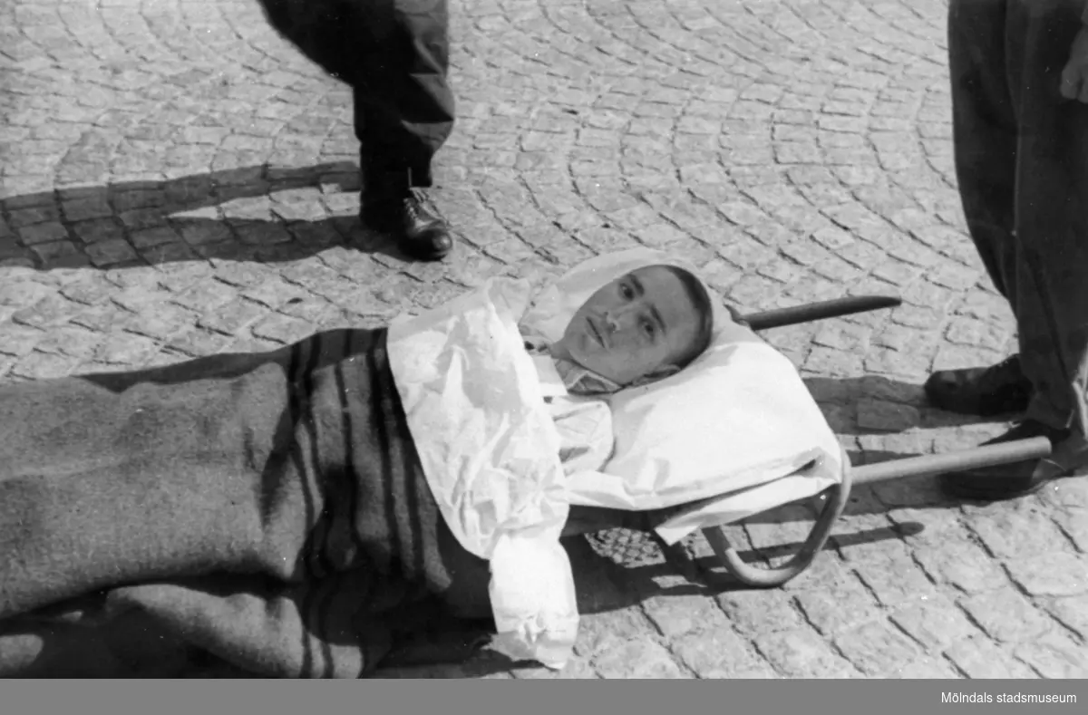"Karantänsförläggning" på Kvarnbyskolan för överlevande från koncentrationsläger i Tyskland och Polen 1945.  
Skolan fungerade under denna sommar som beredsskapssjukhus.

En ung man på bår.