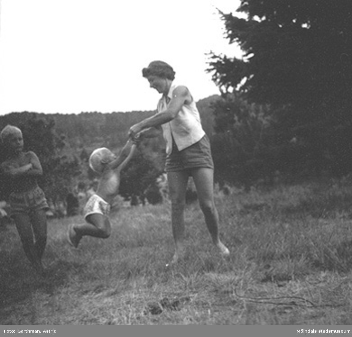 Ulla Torgé svänger runt med sonen Olle Torgé i Mölndal, 1950-tal. Okänt barn tittar på. Vänner till familjen Garthman som är på besök.
